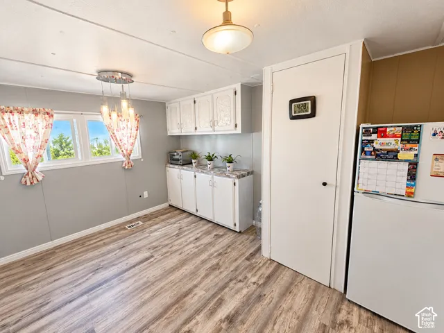 Wood-finish flooring, white built-in cabinetry, multi-pendant light fixture, and windows with natural light