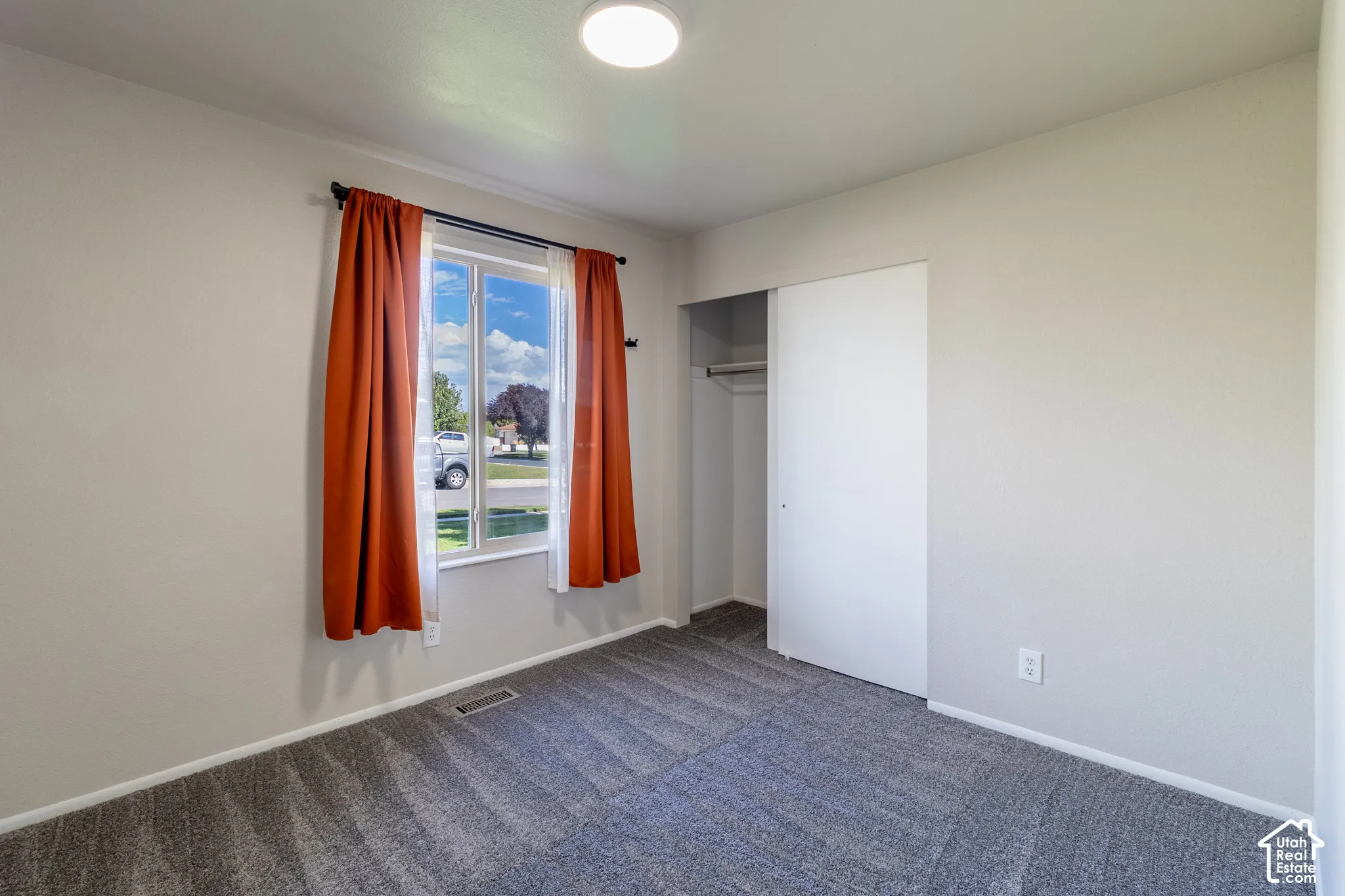 Recessed ceiling lighting, light gray walls, window with white trim, gray patterned carpeting, and white sliding closet doors