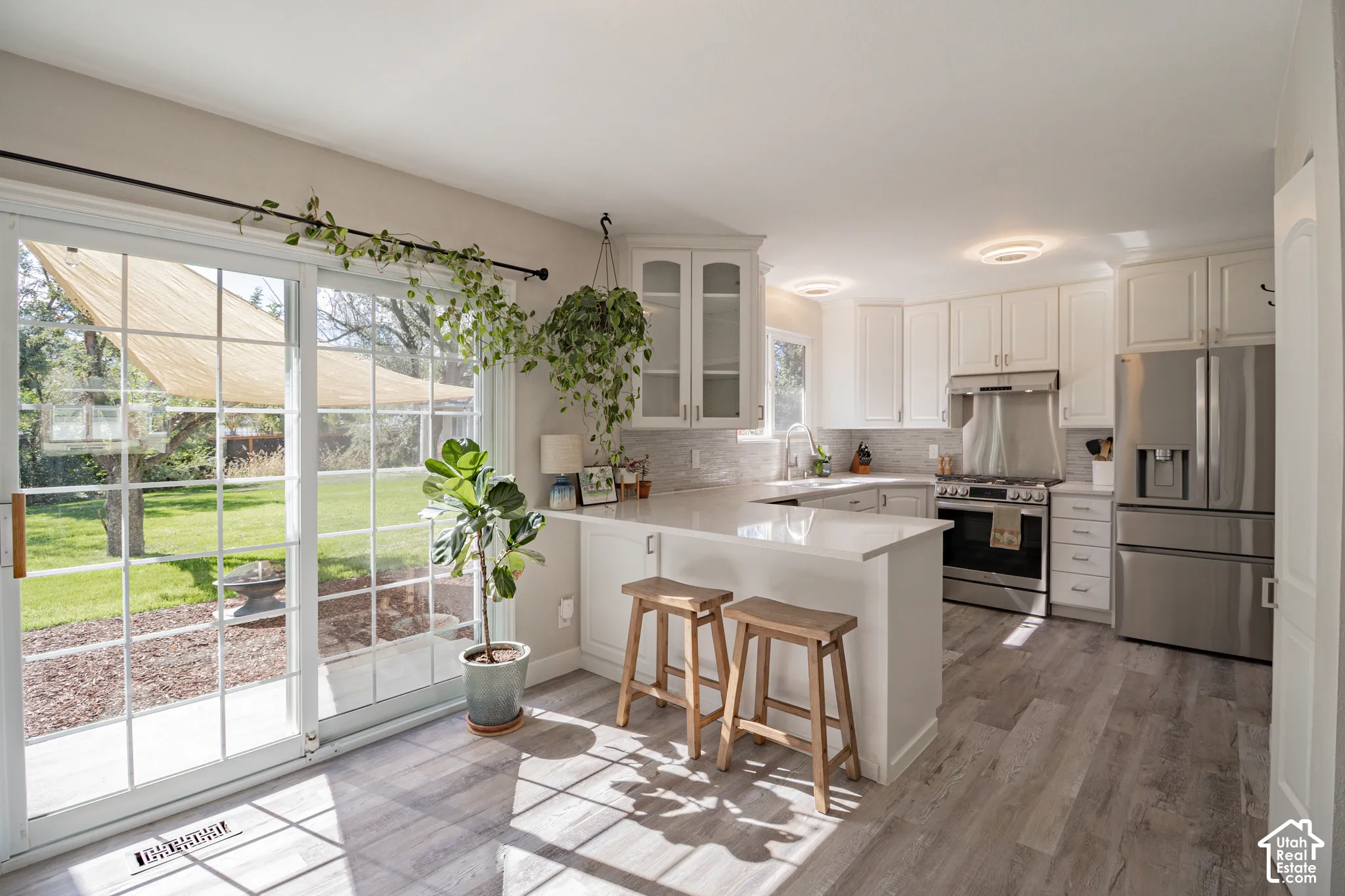 White shaker cabinetry, stainless steel appliances, light-toned wood-finish flooring, white countertops, and a full-height tile backsplash