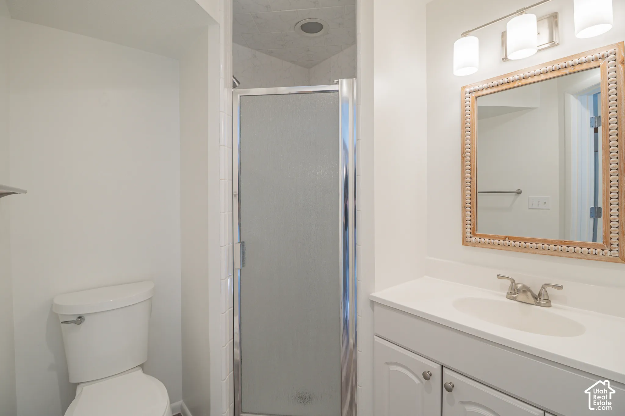 White vanity with an integrated sink and brushed nickel faucet, a decorative framed mirror, and a shower with a clear glass enclosure