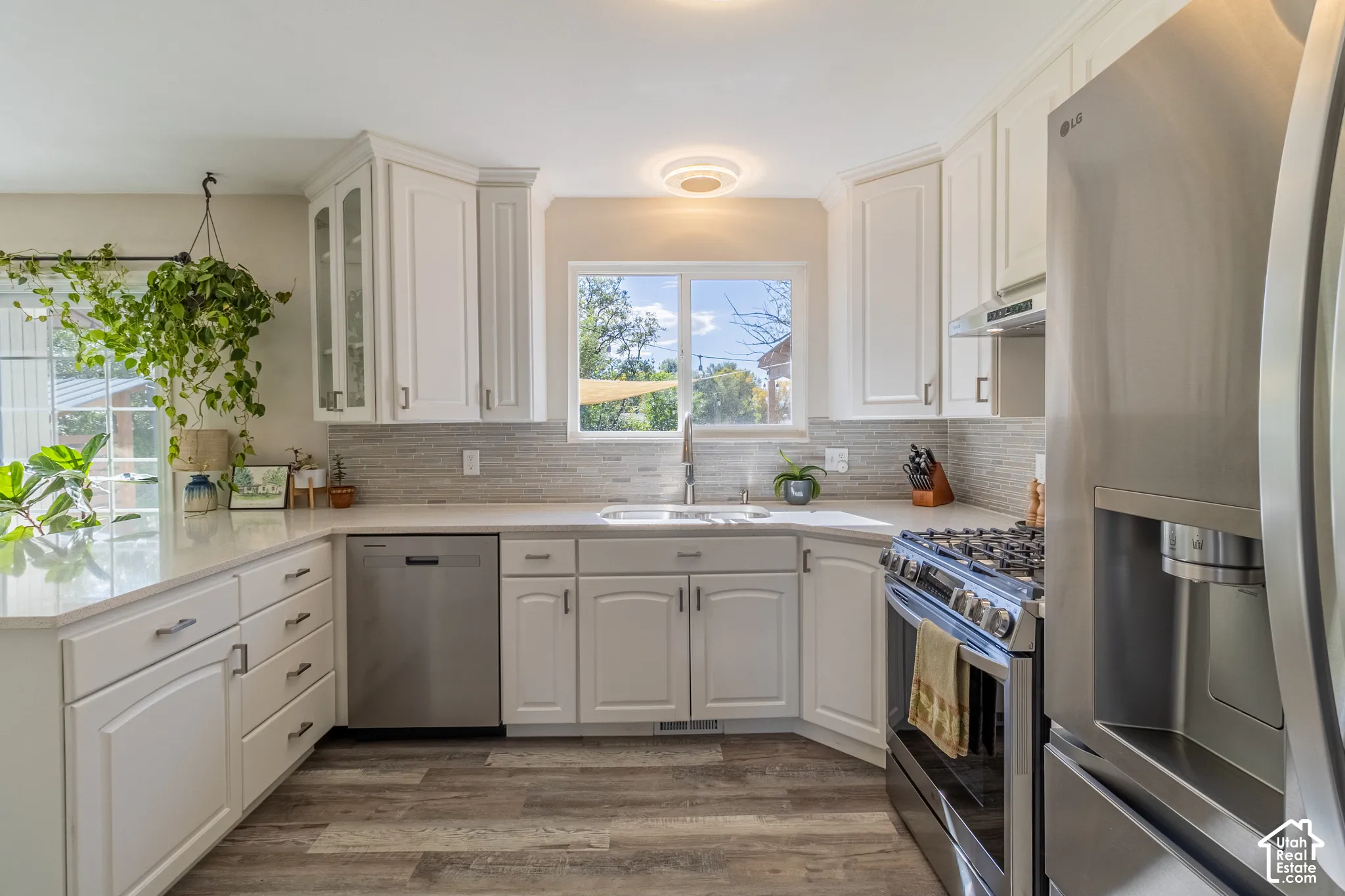 White cabinetry with glass-front accents, stainless steel appliances, wood-finish flooring, and a tile backsplash
