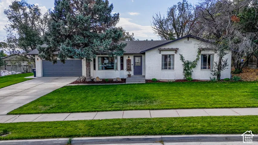 Single-story residence featuring a white brick and siding exterior, an attached garage with a dark gray door, a well-maintained front lawn, and mature trees