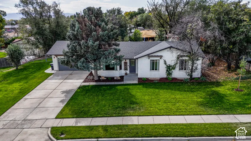 White exterior with dark trim accents, attached garage, concrete driveway, and a level front lawn