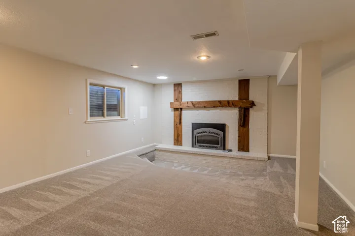 Carpeted room featuring a drop-down floor area, a white brick fireplace with a wood-beam mantel, recessed lighting, and a single window