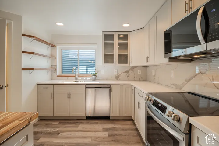 Kitchen featuring stainless steel appliances, stone countertops, wood-finish flooring, white cabinetry, and open shelving