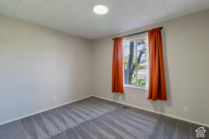 Recessed ceiling light fixture, neutral wall paint, window with white trim, and gray patterned carpeting