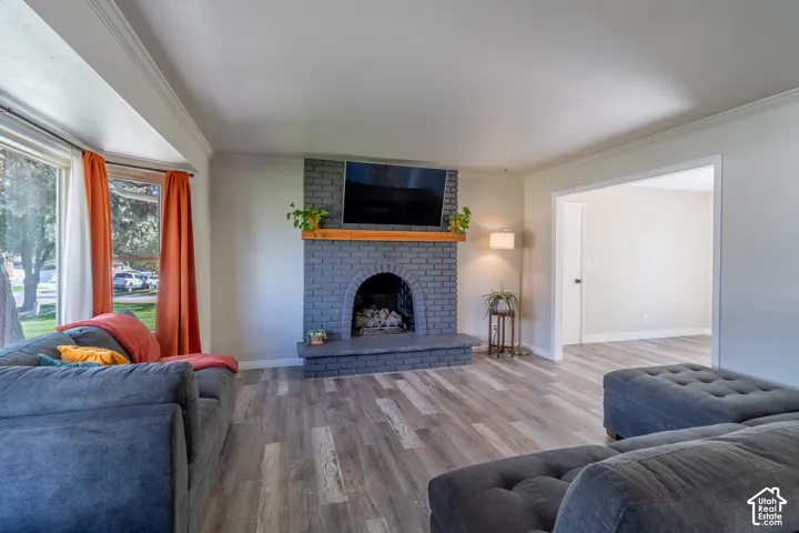 Spacious living area featuring wood-finish flooring, a painted brick fireplace with a wood mantle, and a wide bay window