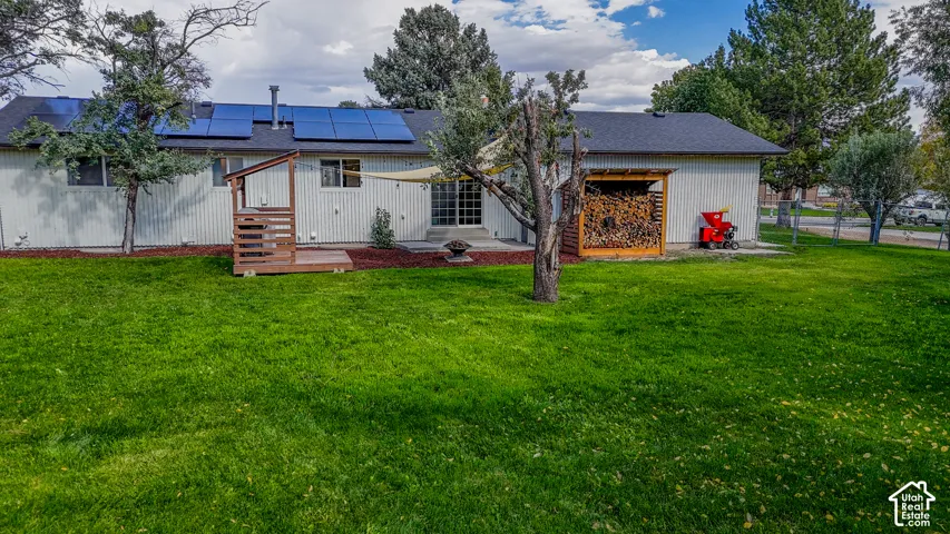 Rear exterior featuring solar panels, a wood deck, a sliding glass door, and a dedicated wood storage structure