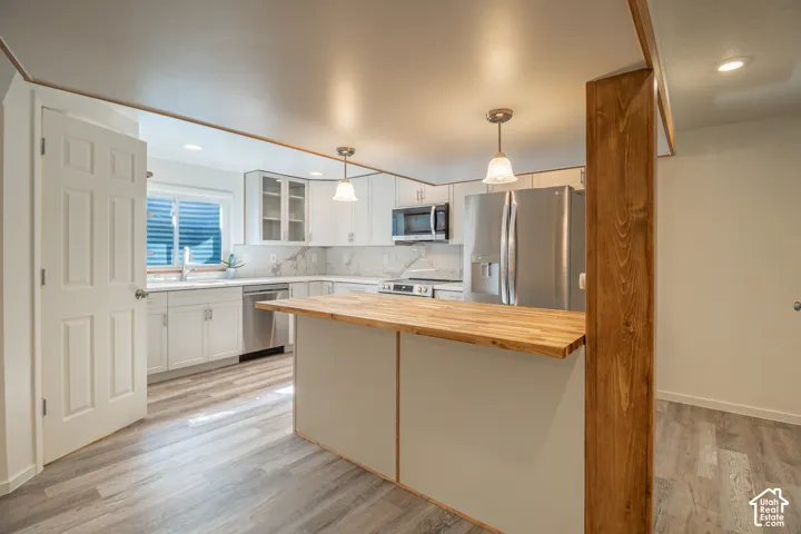 Kitchen featuring white cabinetry, stainless steel appliances, wood-finish flooring, a butcher block island, and pendant lighting