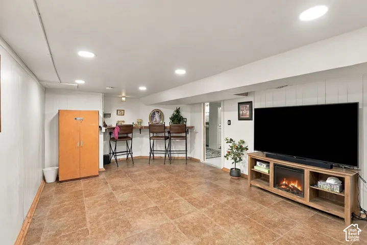 Recessed lighting, large-format tile flooring, vertical wall paneling, and a built-in wooden bar counter