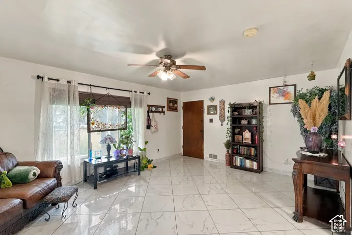 Interior space featuring large-format diagonal tile flooring, a multi-blade ceiling fan with integrated lighting, and a large picture window with adjustable curtain hardware