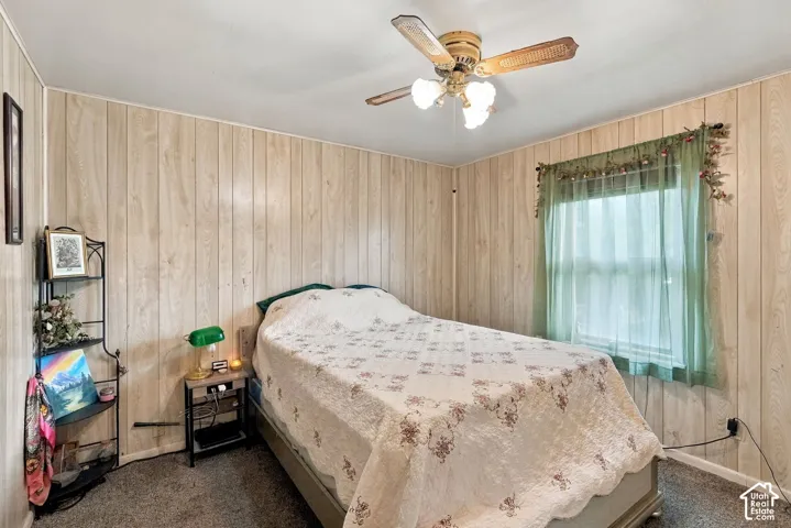 Room featuring wood-paneled walls, neutral carpeting, and a ceiling-mounted fan with integrated lighting