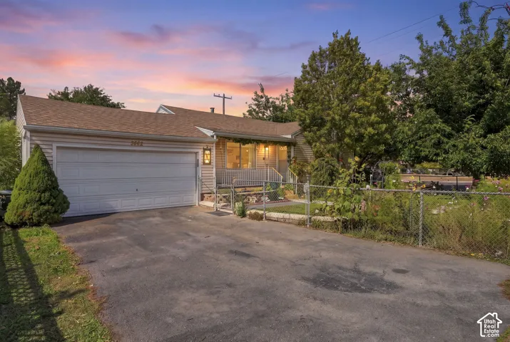 Single-level exterior featuring horizontal siding, an attached two-car garage, a covered front porch with railings, and mature landscaping