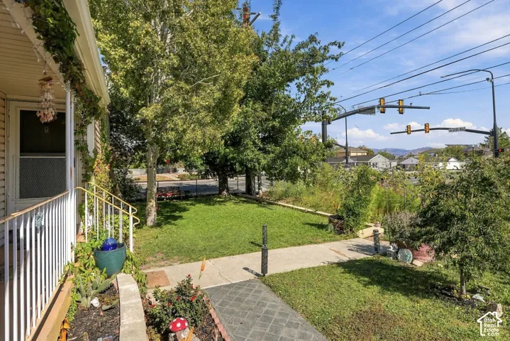 Front yard featuring a concrete walkway, established lawn, mature trees, and a covered porch with white metal railings