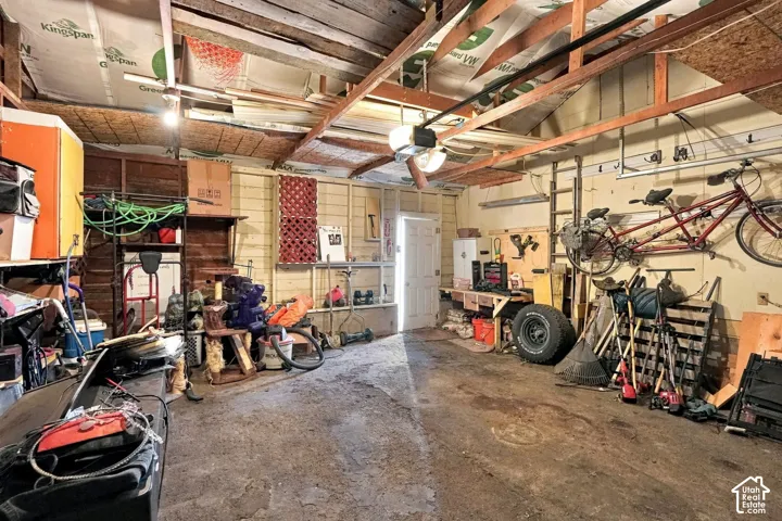 Garage space featuring exposed timber framing, concrete flooring, built-in wooden workbench, and overhead lighting