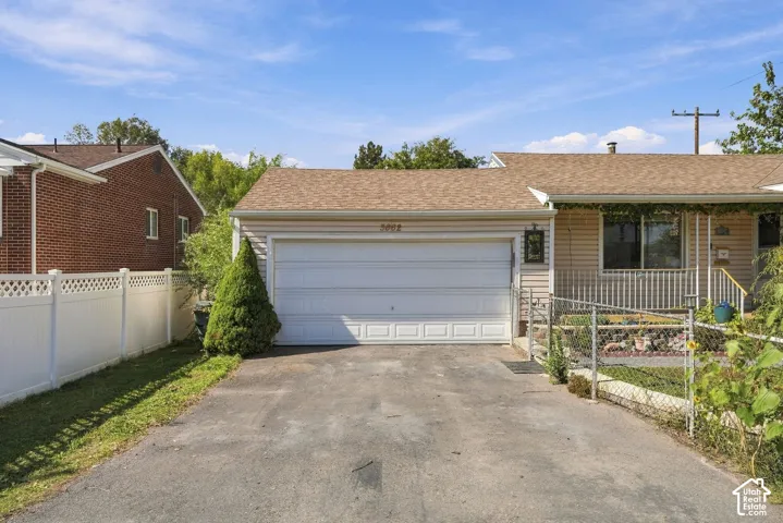 Exterior featuring a two-car garage, asphalt driveway, light-toned horizontal siding, asphalt shingle roofing, and white vinyl privacy fencing