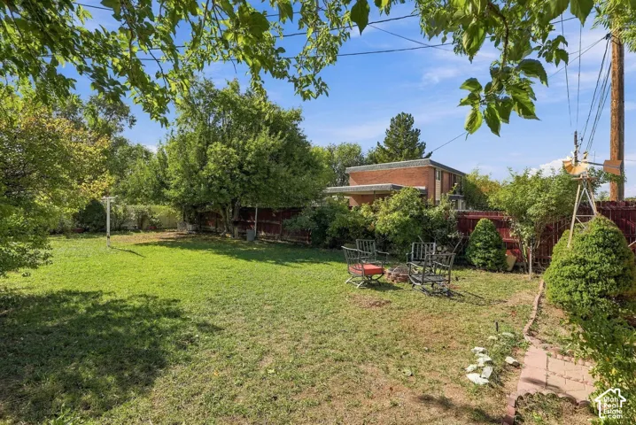 Expansive backyard featuring a grass lawn, mature trees, privacy fencing, and a decorative windmill feature