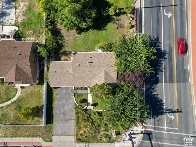 Aerial perspective of a property featuring an asphalt driveway, shingled roofing, mature trees, and landscaped yard space