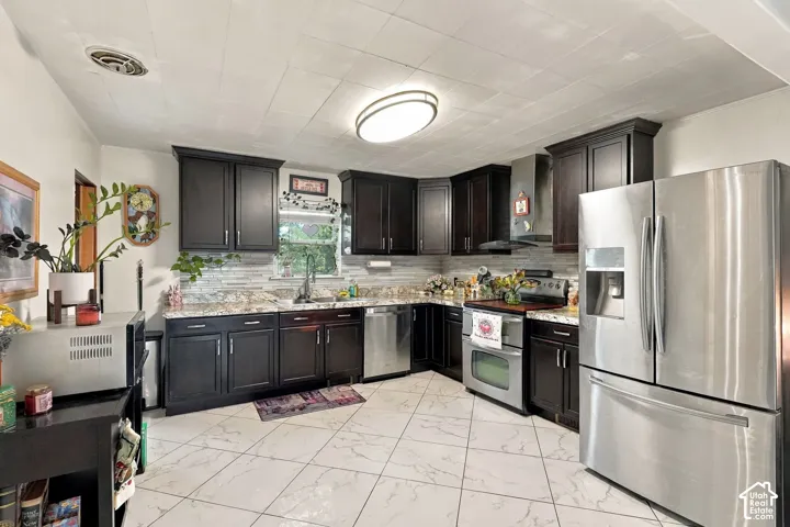 Kitchen featuring dark wood cabinetry, stainless steel appliances, multi-tonal horizontal tile backsplash, stone-finish countertops, and large-format diagonal tile flooring