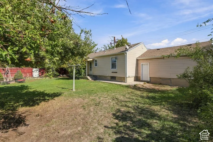 Rear exterior featuring beige vinyl siding, a concrete patio, mature trees, and a red wood fence