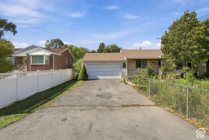 Single-story residence featuring an attached two-car garage, asphalt driveway, vinyl siding, and white lattice privacy fencing