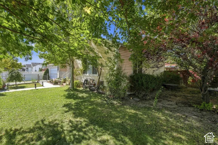 Expansive yard featuring a manicured lawn, mature trees, concrete pathway, and perimeter fencing