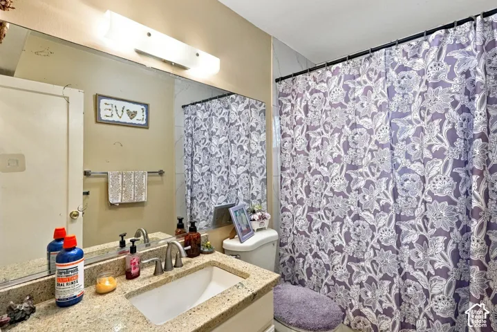 Bathroom featuring a stone-composite countertop, undermount sink, brushed nickel faucet, full-width vanity mirror, and linear wall-mounted lighting