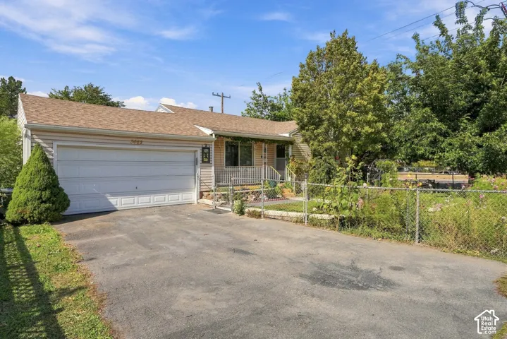 Single-story residence featuring an asphalt driveway, an attached two-car garage, horizontal siding, and a fenced front yard with mature landscaping