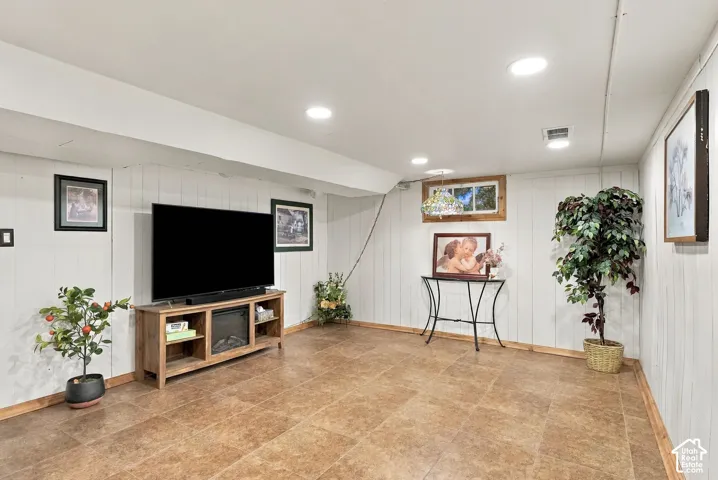 Spacious room featuring paneled walls, tile flooring, recessed lighting, and a window with wood-trim framing