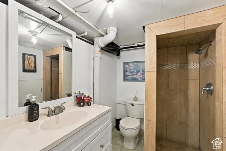 Bathroom featuring a white vanity with a composite countertop and integrated basin, a framed mirror, a tiled shower stall with an adjustable showerhead, and a ceramic toilet