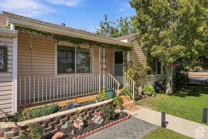 Exterior siding, covered porch with metal railing, stacked-stone garden edging, concrete walkway, and mature landscaping