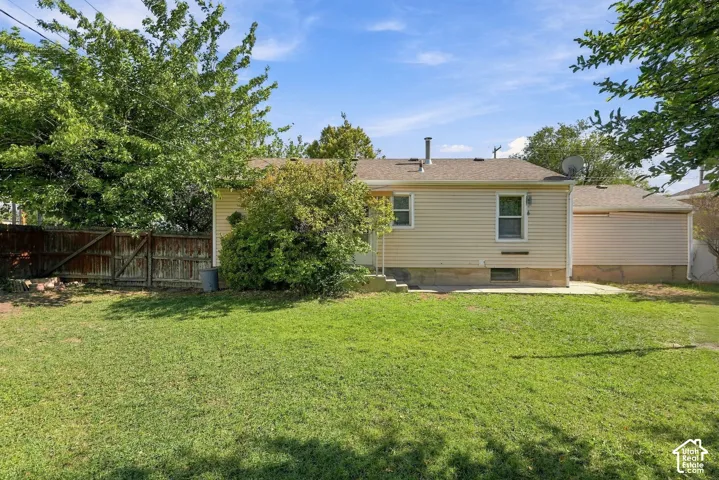 Exterior rear elevation featuring horizontal siding, a concrete patio, mature trees, and a wood privacy fence