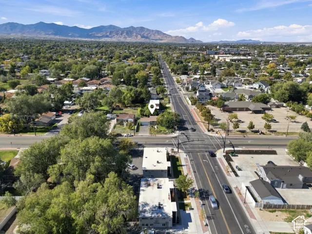 Aerial perspective of residential property featuring a composition shingle roof, asphalt driveway, and mature landscaping, set against a mountainous horizon