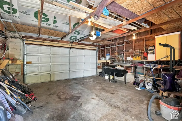 Multi-car garage featuring a sectional overhead door, exposed wood-joist ceiling, concrete floor, and integrated wall-mounted storage shelving