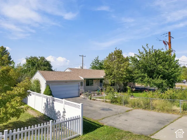 Single-story residence featuring horizontal siding, an attached two-car garage, an asphalt driveway, and perimeter white vinyl fencing