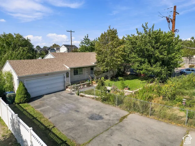 Rambler-style exterior featuring a multi-car paved driveway, attached two-car garage, shingle roof, and mature trees on the property grounds