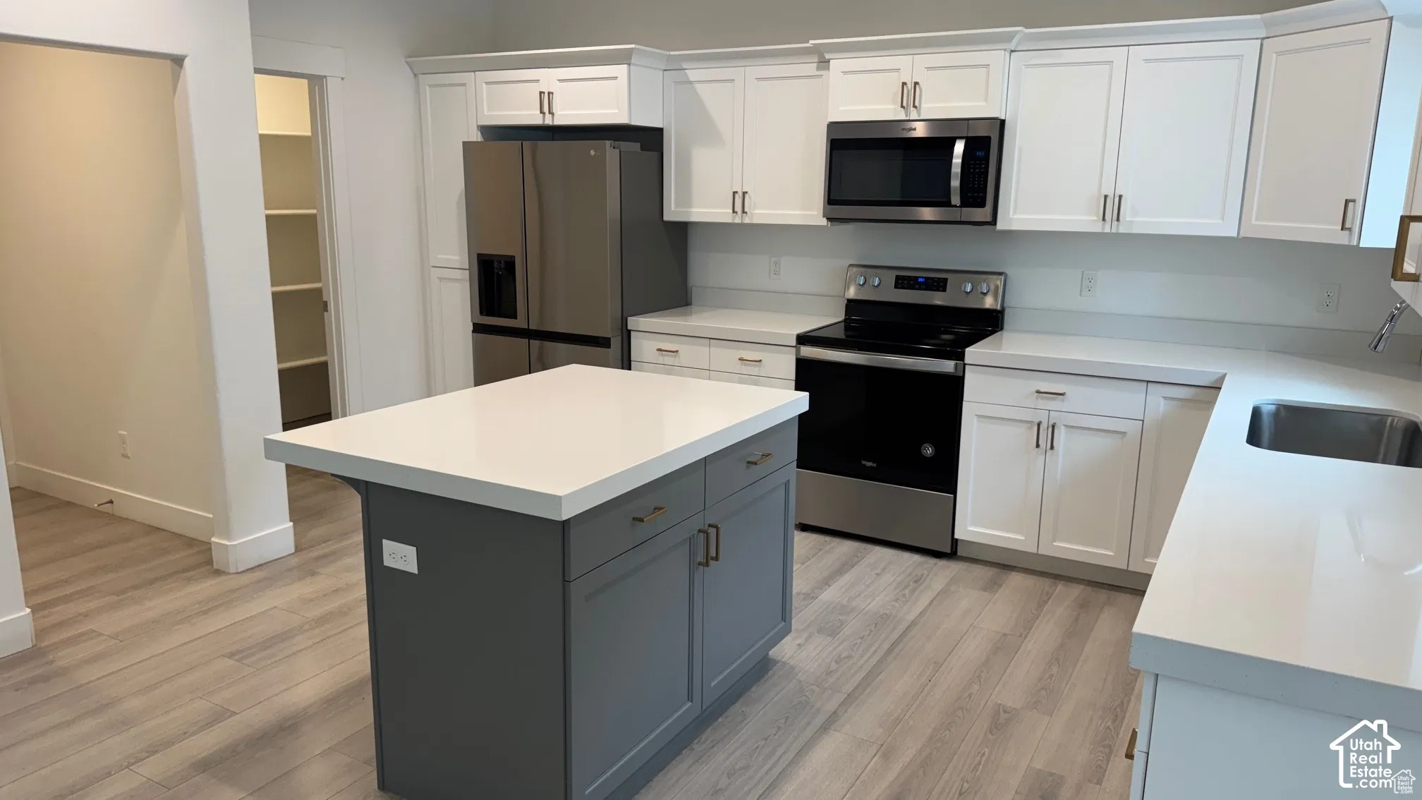 Modern kitchen featuring white cabinetry, a gray island with a light-toned countertop, stainless steel appliances, and light wood-finish flooring