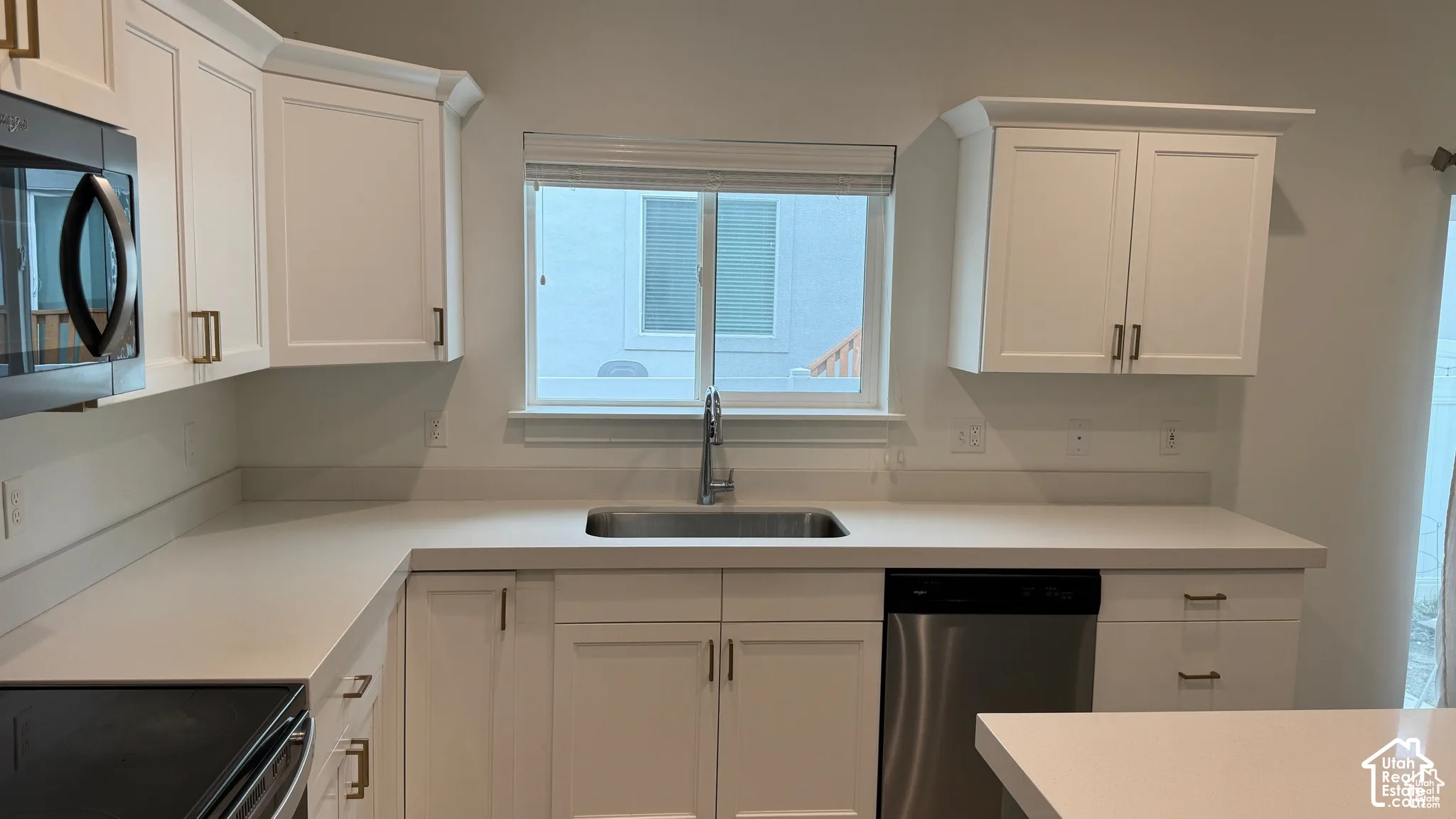 Kitchen featuring white cabinetry, light-toned countertops, a stainless steel sink with a gooseneck faucet, a stainless steel dishwasher, and a built-in microwave