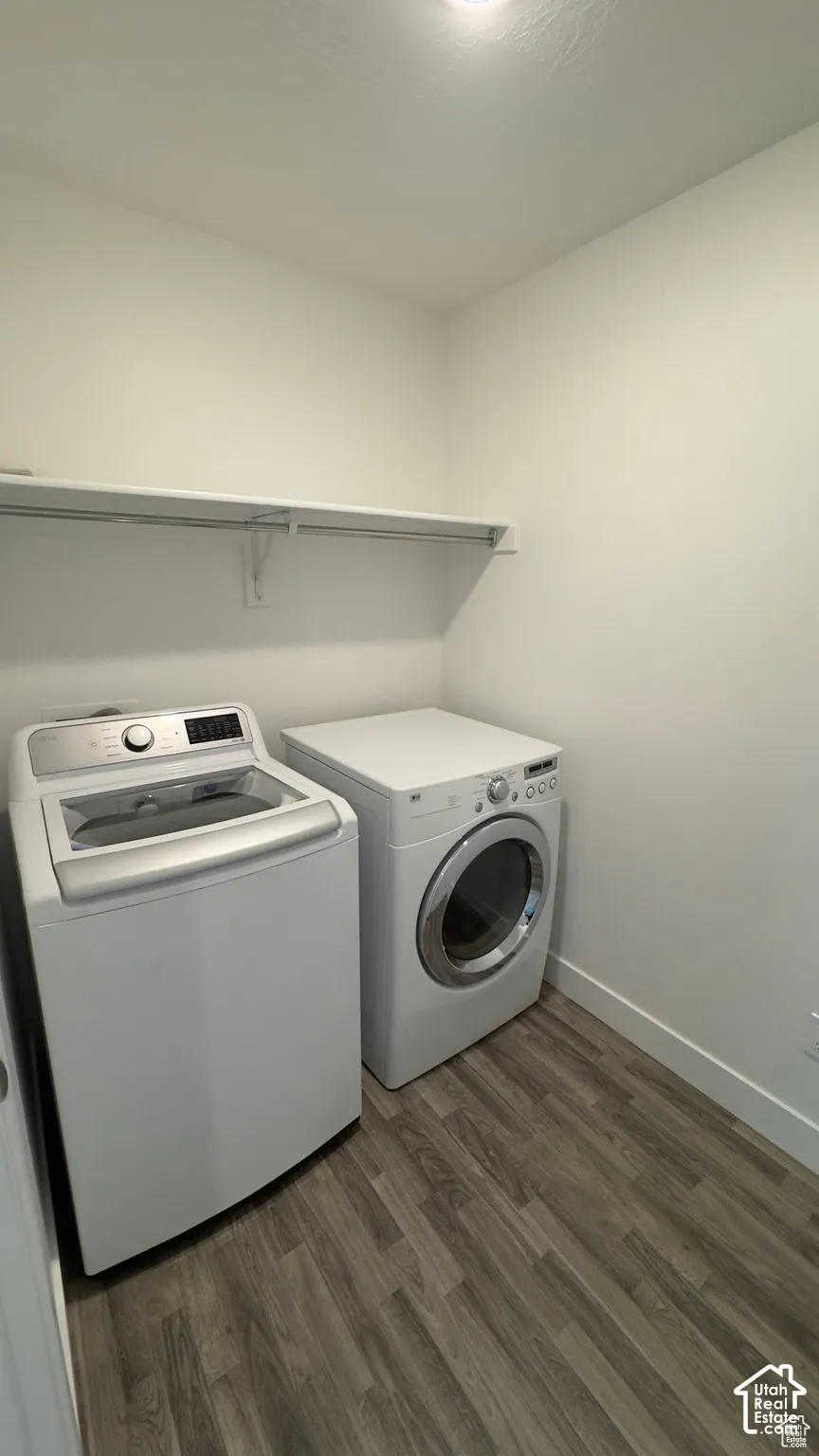 Integrated laundry area featuring wood-finish flooring, a white shelving unit, and white walls