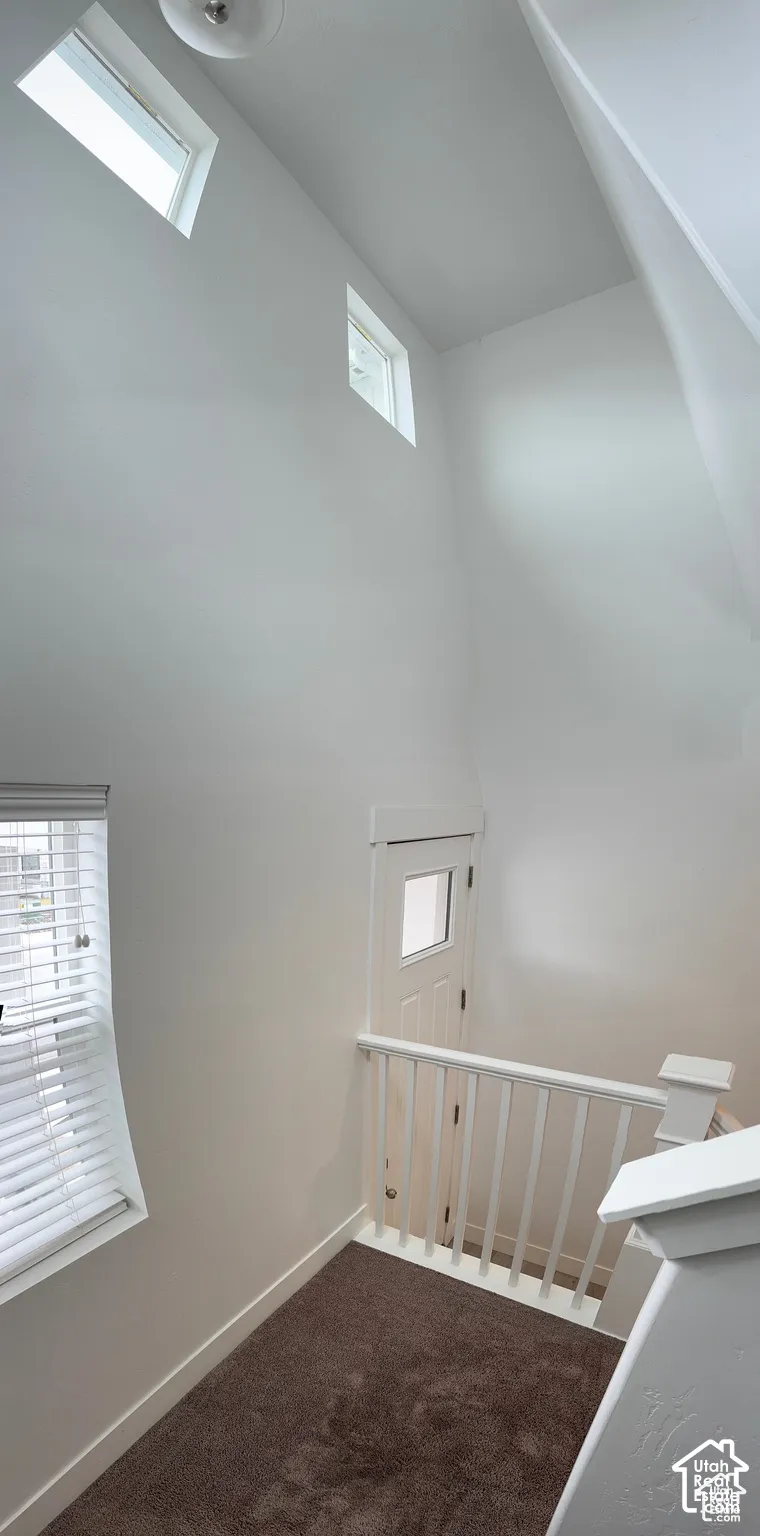 Vaulted ceiling with high windows, natural light, carpeted flooring, and white painted railings