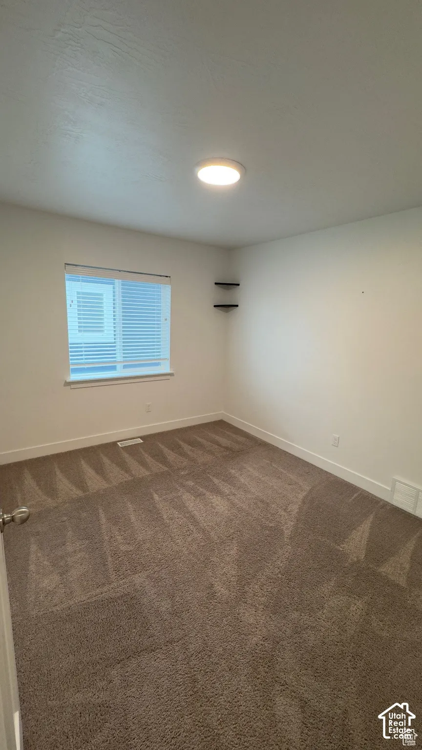 Neutral tone wall paint with white trim, brown patterned carpeting, window with blinds, and ceiling-mounted flush light fixture