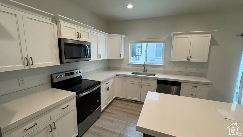 White shaker cabinetry with crown molding, stainless steel appliances, light-toned countertops, undermount sink with a gooseneck faucet, and wood-finish flooring