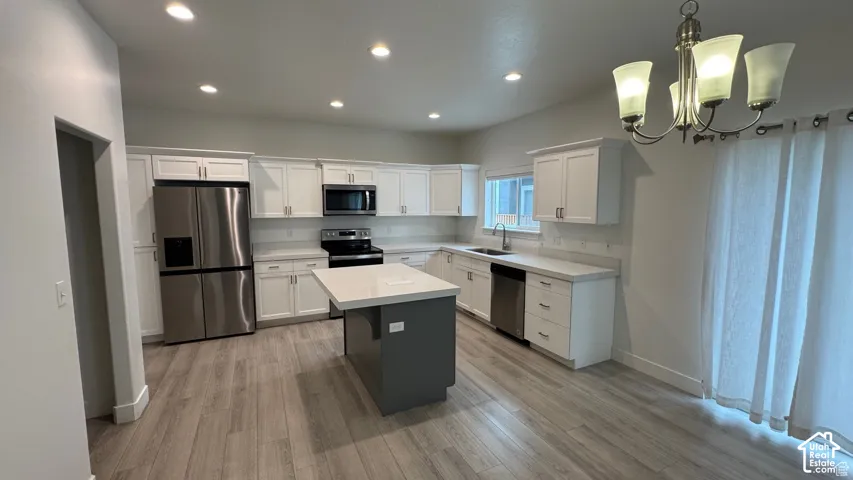 Modern kitchen featuring white cabinetry, stainless steel appliances, a center island with a white countertop, and wood-finish flooring