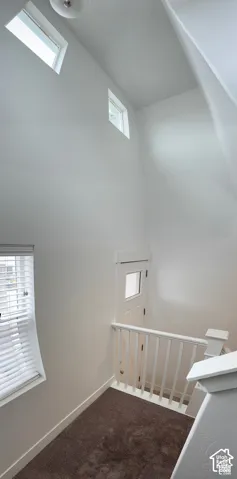 Vaulted ceiling with high windows, natural light, carpeted flooring, and white painted railings