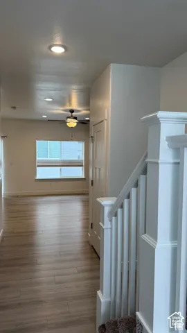 Wood-finish flooring throughout, recessed ceiling lighting, ceiling-mounted fan with light fixture, and white painted balusters and newel post