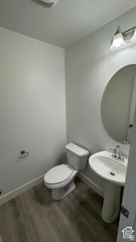Pedestal sink with chrome faucet, oval mirror, toilet, and wood-finish flooring