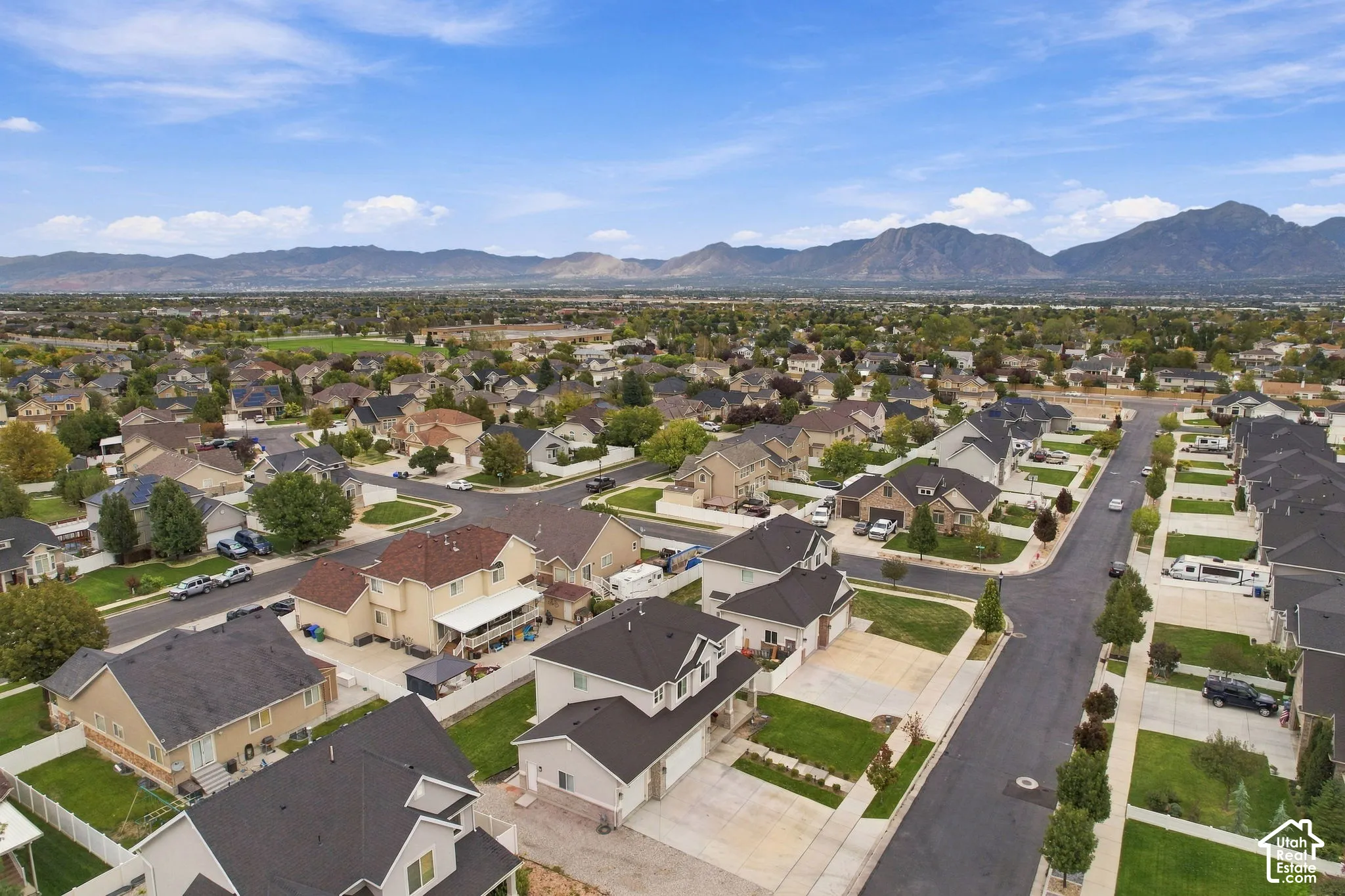 Aerial perspective of a suburban neighborhood featuring paved street grids, manicured lawns, multi-story single-family residences with pitched rooflines, and a backdrop of mountain ranges