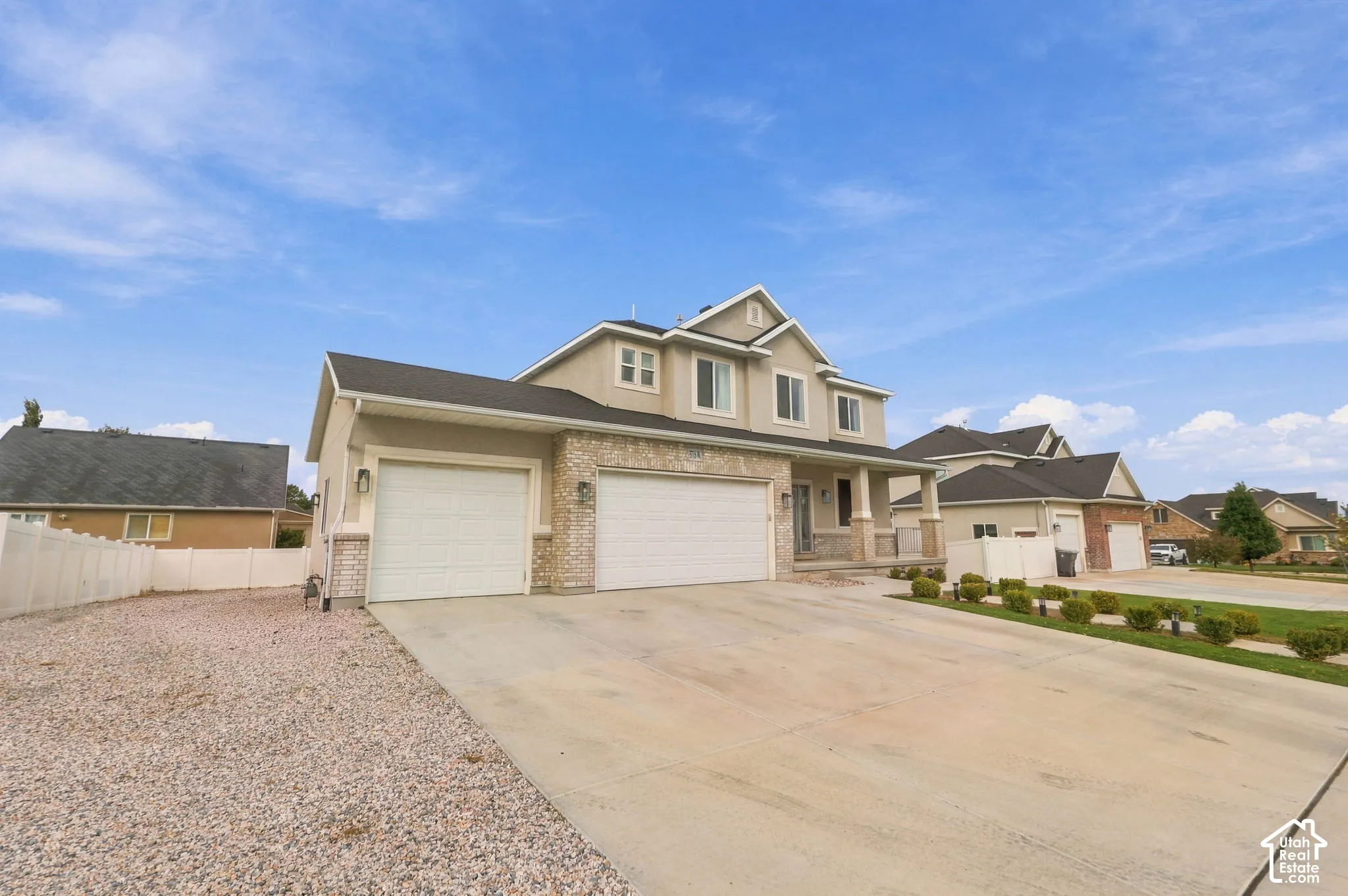 Multi-level exterior featuring stone veneer accents, a triple-car garage, concrete driveway, and a white privacy fence