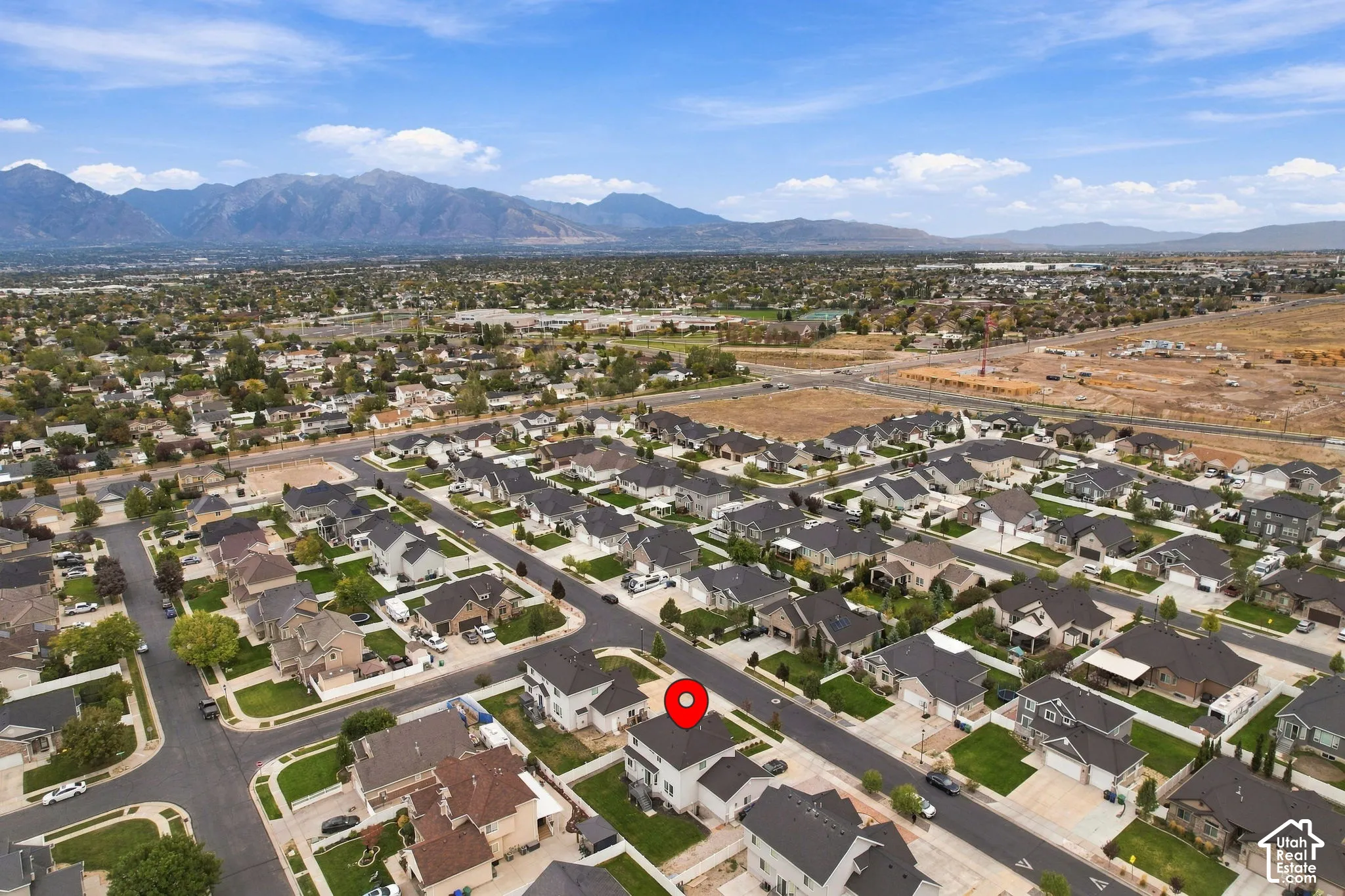 Aerial perspective featuring a two-story residence with a multi-gabled roofline and an attached garage, situated on a lot with a fenced backyard and a mountain backdrop
