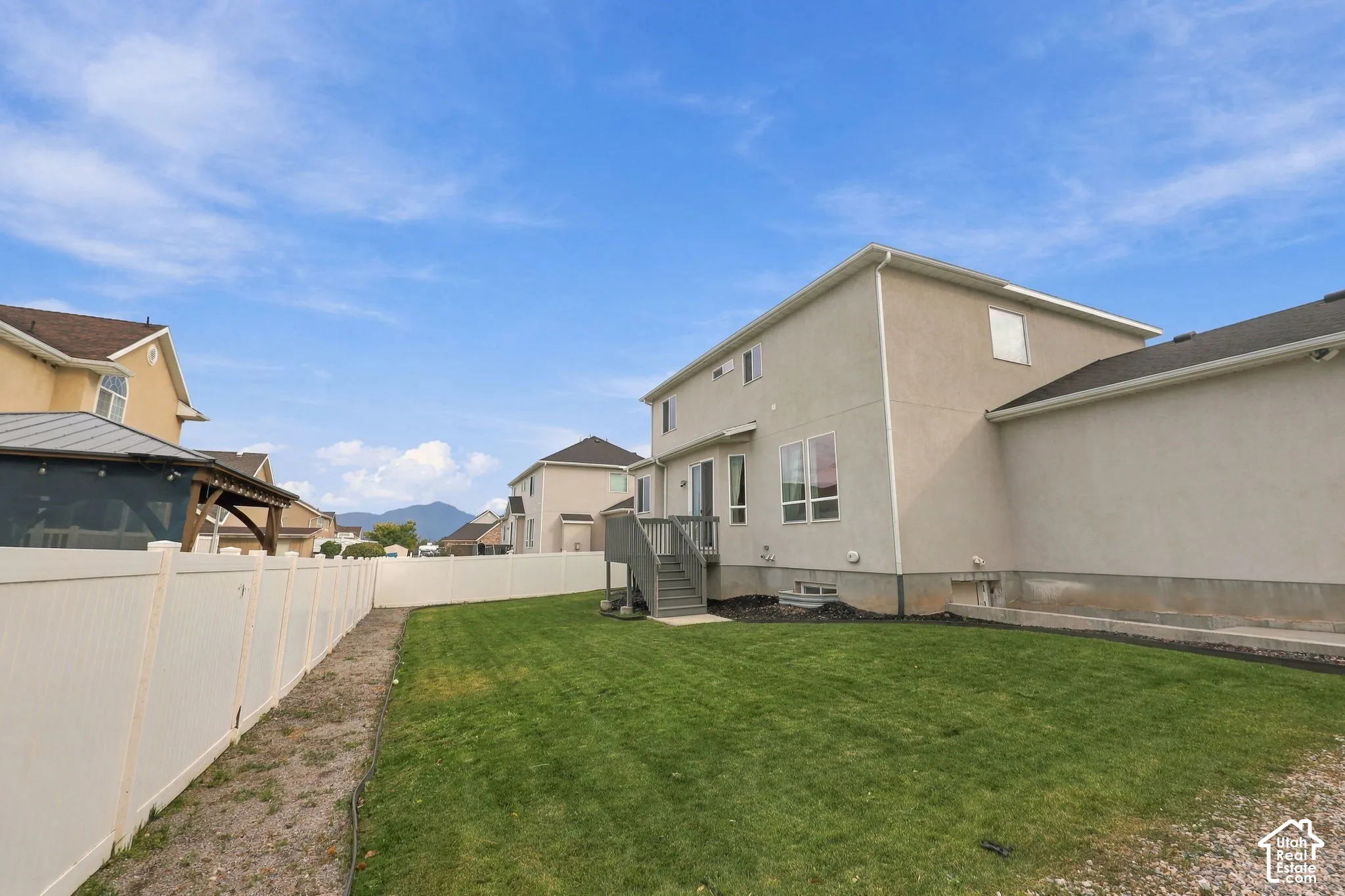 Rear exterior featuring a stucco facade, elevated wood deck with stairs, vinyl privacy fencing, and a grass lawn